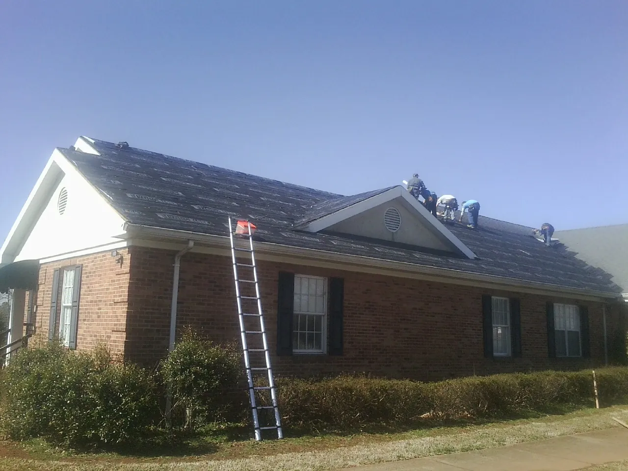 Crew tearing shingles off a brick ranch roof with a ladder set — Metal Roof Repair work by our crew in Barrington